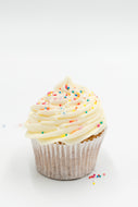 A beautifully frosted vanilla cupcake, topped with a generous swirl of creamy white frosting and sprinkled with colorful candy sprinkles. The cupcake is set against a clean, white background, emphasizing its simple yet elegant appearance. The smooth, fluffy frosting and moist cupcake base suggest a deliciously sweet and classic treat, perfect for any occasion or celebration.